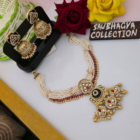 antique gold tone green stone necklace set, traditional green centerpiece necklace with maroon accents, ivory pearl bead necklace with matching jhumka earrings, antique gold necklace with white teardrop stones, traditional artificial jewellery set for women, green stone ethnic necklace with maroon bead border, gold tone necklace with pearl-like hanging details, Indian wedding necklace set with matching earrings