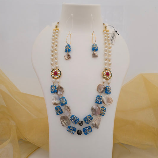 Blue and pearl white necklace mala featuring patterned blue beads, multiple pearl-style strands, pink centre stone accents, irregular beige and grey beads, black decorative beads and matching earrings displayed on a white jewellery bust