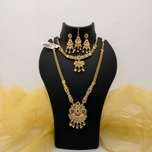 Gold plated short and long necklace combo set featuring intricate floral motifs, an ornate statement pendant, green red and white decorative stones, pearl-drop embellishments, matching earrings and maang tikka displayed on a black jewellery bust
