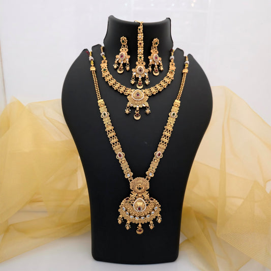 Gold plated short and long necklace combo set featuring intricate floral designs, ornate statement pendants, pink green and white decorative stones, matching earrings and a traditional maang tikka on a black jewellery display