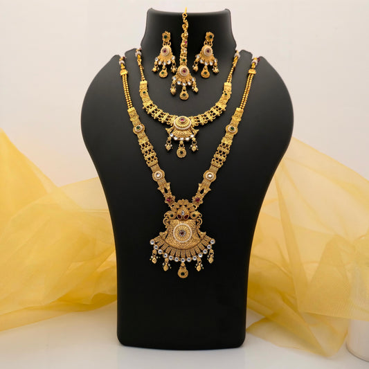 Gold plated short and long necklace combo set featuring intricate traditional ornamental designs, a large statement pendant, red green and white stone accents, matching earrings and maang tikka displayed on a black jewellery bust