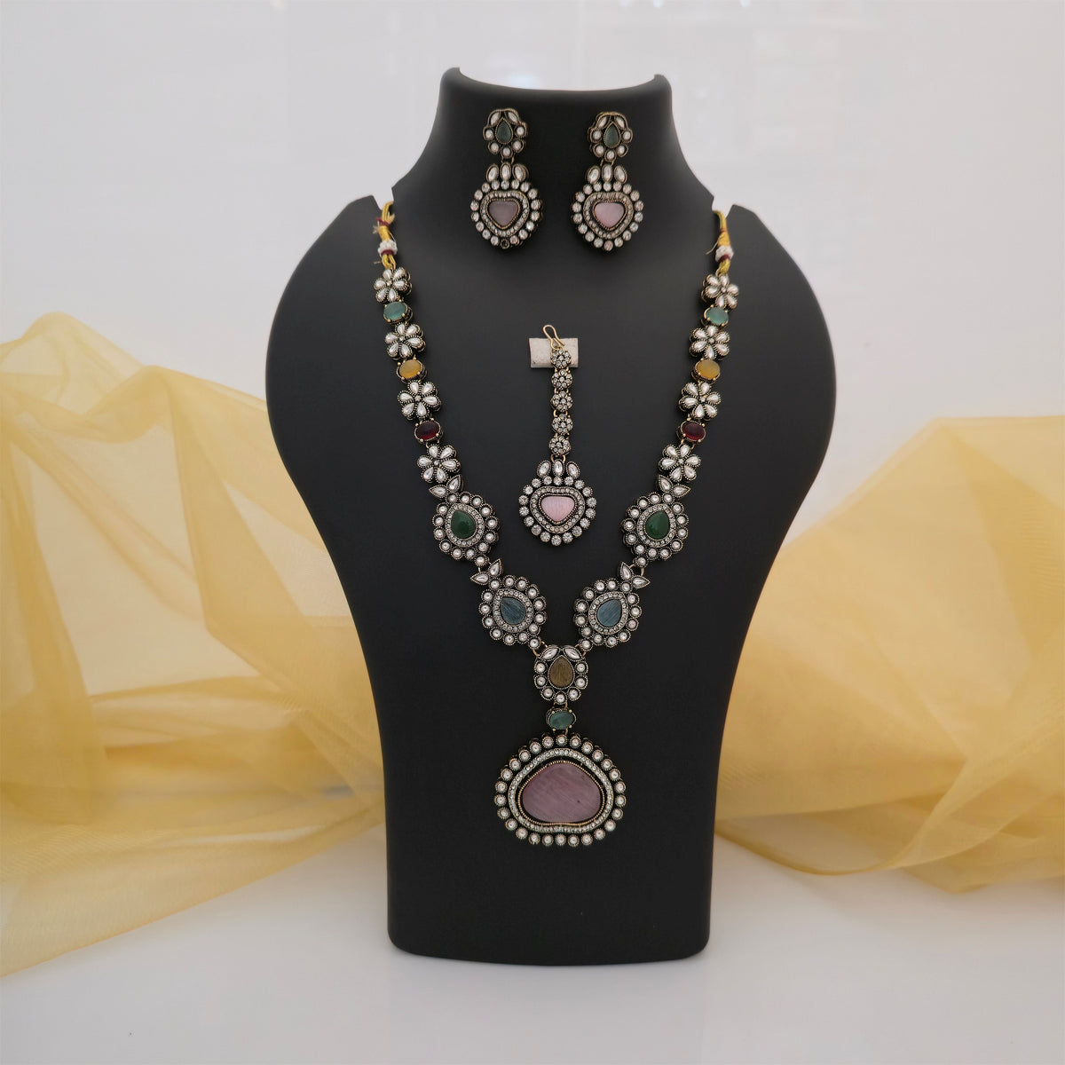 multicolour Moissanite and AD necklace set with matching earrings and maang tikka, pink heart pendant designer necklace for women, green blue and pink stone ethnic jewellery set, antique gold-tone floral necklace with white stones, traditional statement necklace set for weddings, multicolour festive jewellery for women, Scofjewel designer necklace set