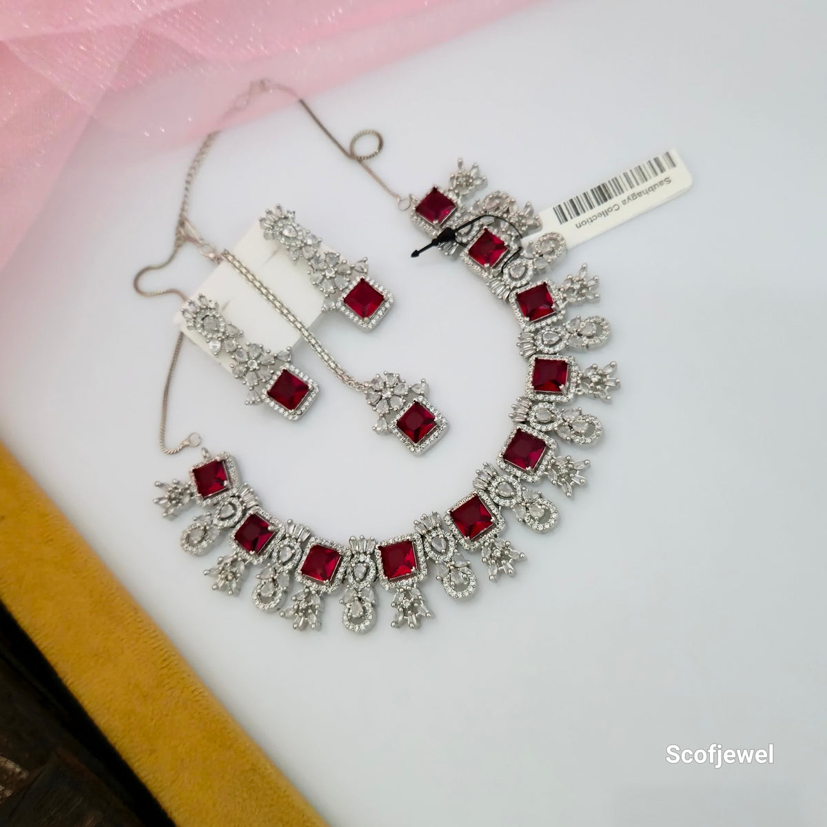 ruby red square stone necklace set with matching earrings and maang tikka, red square stone designer necklace for women, silver tone traditional jewellery with floral detailing, ruby red wedding necklace set, artificial stone necklace with white accents, red ethnic jewellery set for festive occasions, statement necklace with matching accessories, Scofjewel ruby red necklace set