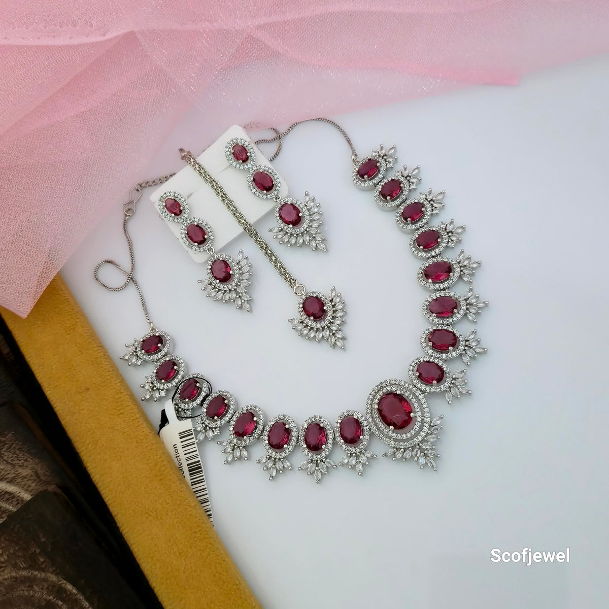 ruby red stone necklace set with matching earrings and maang tikka, red oval stone designer necklace for women, silver tone traditional jewellery set with white accents, ruby red wedding necklace set, elegant red ethnic jewellery for women, statement necklace with matching accessories, Scofjewel red stone jewellery set